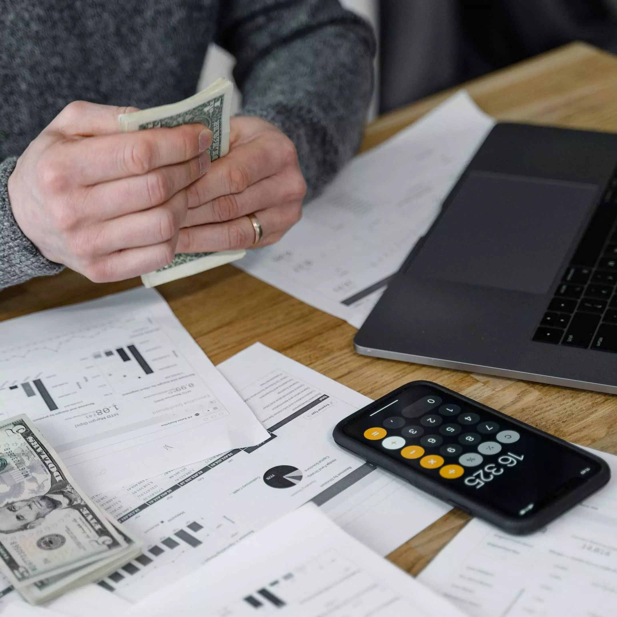 Image of a person sitting at a desk counting cash with a calculator and laptop visible